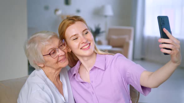 Young daughter teaches elderly mother taking selfie on smartphone at home alt