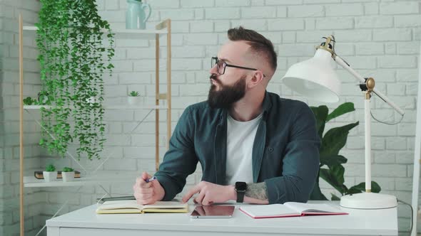 Bearded Man Learn Online Courses Using a Tablet and Write Notice in His Notebook alt