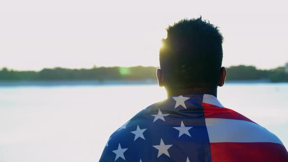 Afroamerican Man with American Flag on Shoulders Looks Into Distance at Sunrise alt
