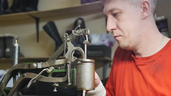 a Male Shoemaker Adjusts a Sewing Machine for Sewing Shoes with a Strong Thread