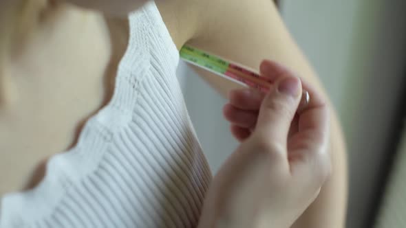 The girl inserts a glass thermometer in the armpit. Body temperature measurement alt