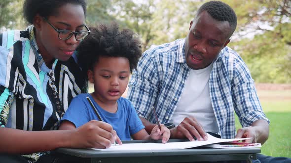 Happy African American Parents enjoy with son to drawing during picnic in the park