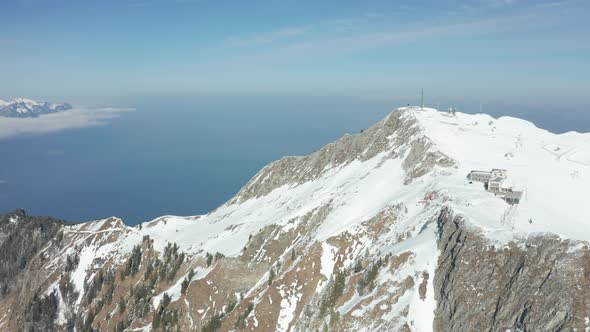 Aerial of several buildings with radio tower on top of snow covered mountain alt