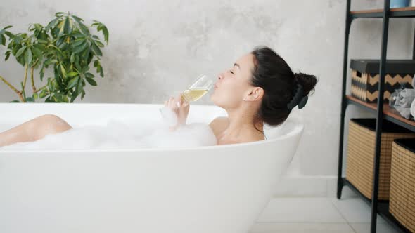 Beautiful Lady Drinking Champagne Smiling Relaxing in Bathtub Indoors at Home alt