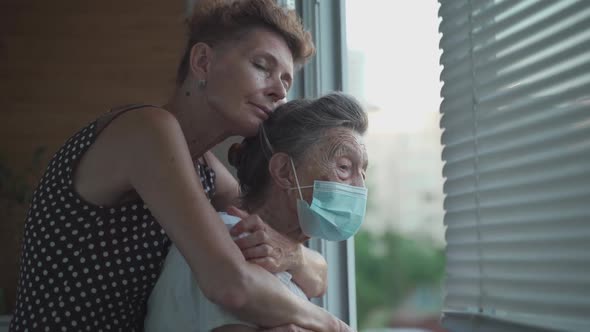 Lonely Senior Woman 90 Years Old in Medical Mask and Her Mature Daughter Standing in Embrace Looking alt