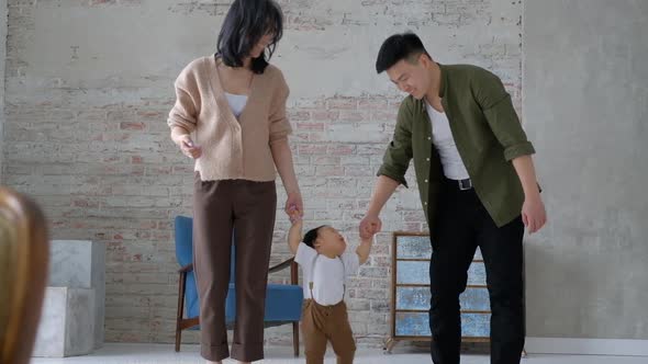 First step. Loving young parents hold hands of an innocent baby inside the room alt