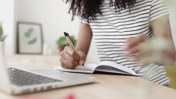 Cheerful African American Woman Using Laptop While Taking Notes in Notebook alt
