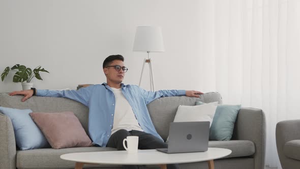 Young Man in Glasses Sitting on Couch Taking Break in Online Work at Home Slow Motion alt