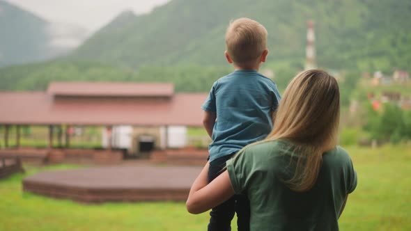Woman Holds Little Son Showing Distant Mountains in Hotel alt