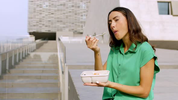 Young woman eating lunch in front of modern building