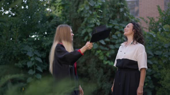 Excited Grad Woman Throwing Graduation Cap Up in Slow Motion with Cheerful Mother Smiling Clapping alt
