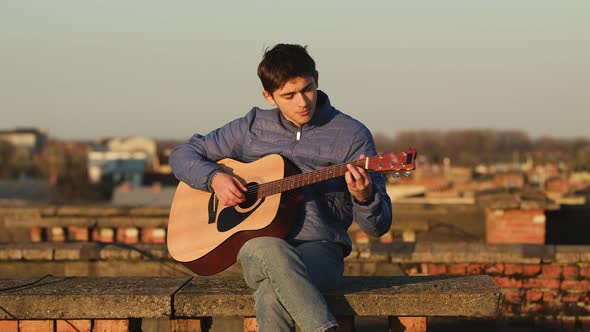 Young Guy in the Sunset Plays Guitar on the Roof of the House. Freedom Concept alt