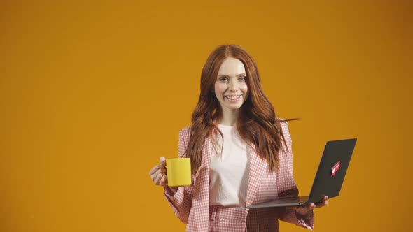 Portrait of a Young Woman with Long Red Hair with a Laptop and a Mug in Her Hands on an Isolated