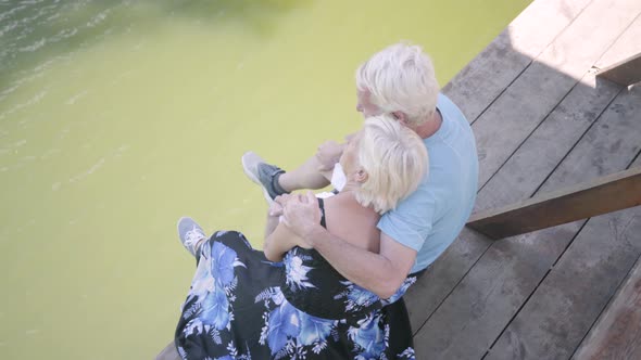 Top View of a Happy Mature Couple Sitting on the Bench Near the River, Admiring Nature alt