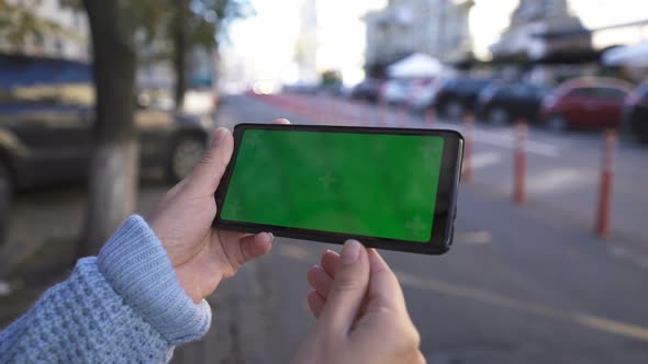Girl Uses a Phone with a Green Screen on the Street. Scrolling Pages