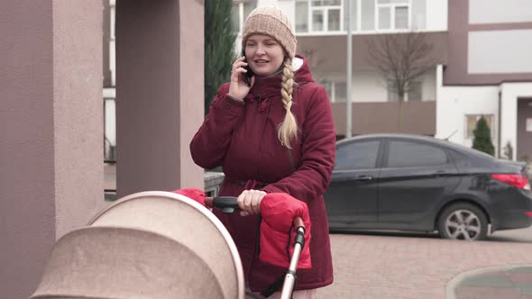 Young Mom Walks Outdoors With A Stroller And Talking To Her Friends On