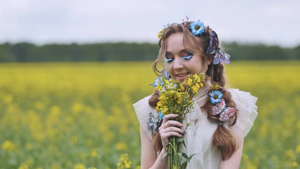 A Young Girl Poses in a Rapeseed Field with a Beautiful Hairdo of Flowers and Butterflies alt