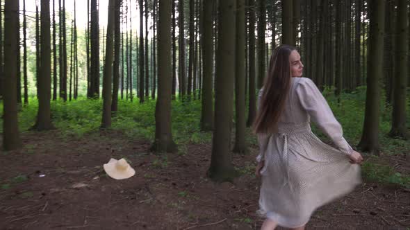 A Woman in a White Dress Whirls in the Forest Around a Straw Hat