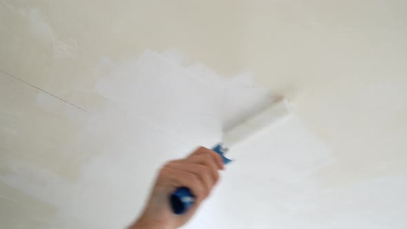 A Worker Paints The Ceiling With White Paint