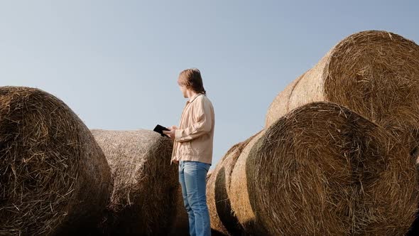 Farmer Agronomist Checks Hay Bales on the Wheat Field After Harvest at Sunset alt