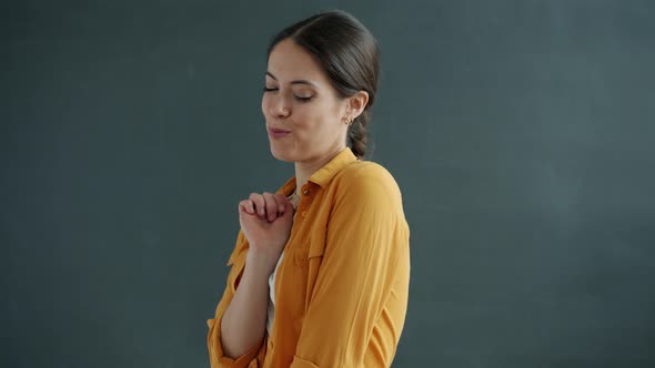 Slow Motion of Shy and Romantic Girl Waving Hand and Winking Flirting on Gray Background alt