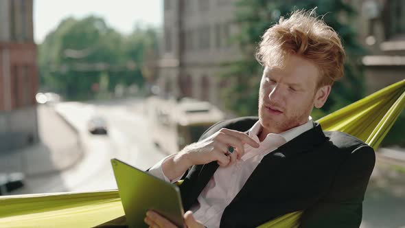 Man in Suit Lying in Hammock with Tablet and Feeling Hot alt