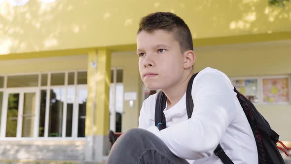 A Caucasian Teenage Boy Thinks About Something As He Sits in Front of School  Closeup