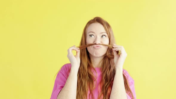 Happy female grimaces on an isolated yellow background playing with long hair