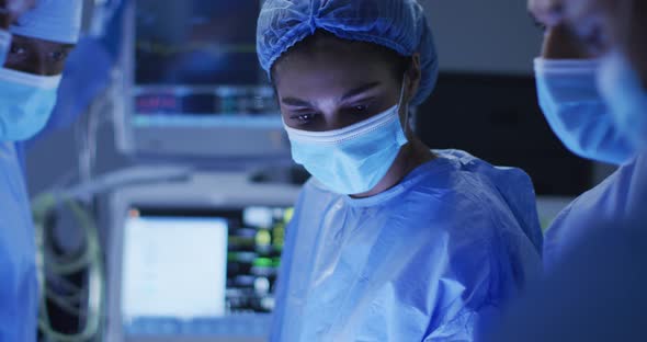 Mixed race surgeons wearing protective clothing discussing in operating theatre alt