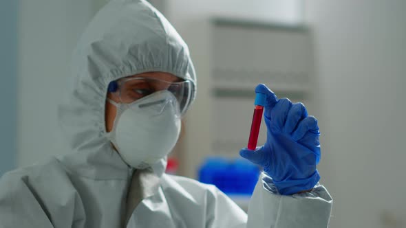 Biochemist in Coverall Holding Blood Sample Analysing Chemical Reaction alt