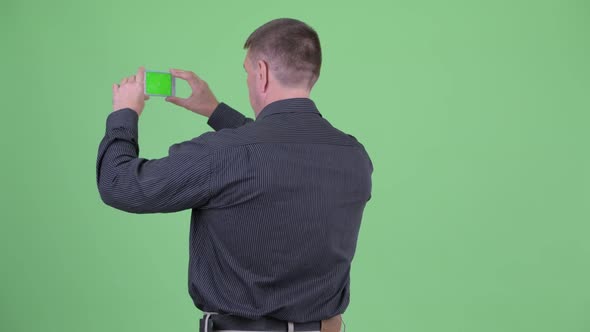 Rear View of Macho Mature Businessman Taking Picture with Phone alt