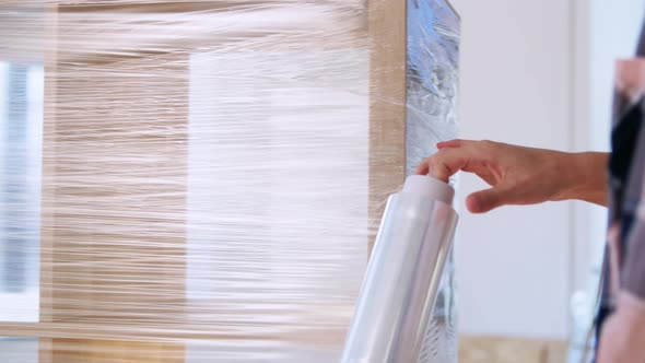 Woman Packing Shelf with Plastic Wrap at Home