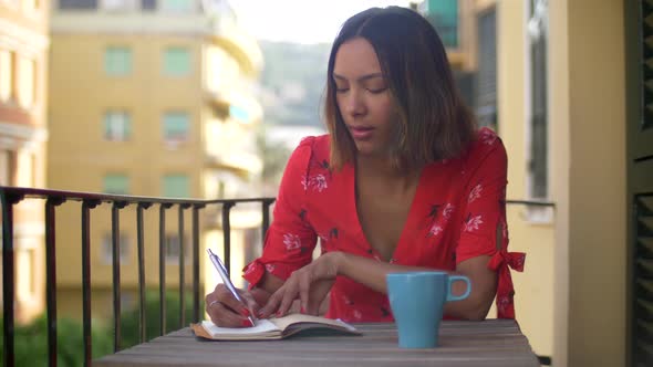 A woman writing in a journal diary traveling in a luxury resort town in Italy, Europe. alt