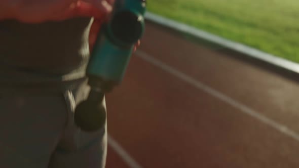 A Male Athlete Massages Muscles and Tendons with a Massage Percussion Device After a Workout at the alt