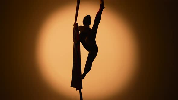 Silhouette of a Young Woman Performs Acrobatic Elements on Airy Silk alt