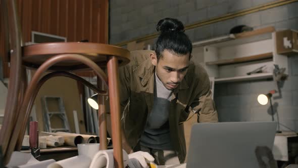 Young Asian man Carpenter uses a tape measure to measure chair on the workbench