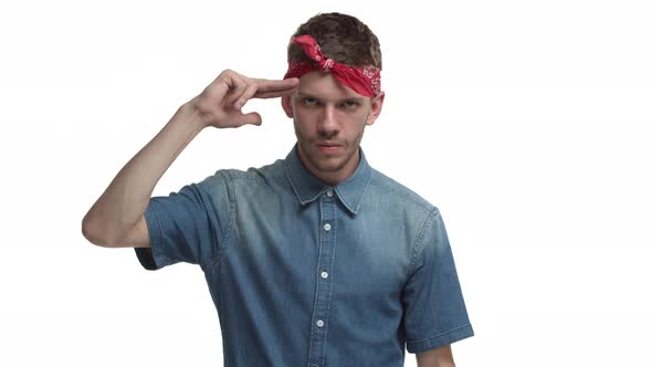 Sassy Handsome Guy with Beard Red Bandana Over Forehead Making Finger Gun Sign Over Head and