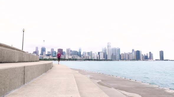 Young woman jogging in Chicago with skyline on background alt