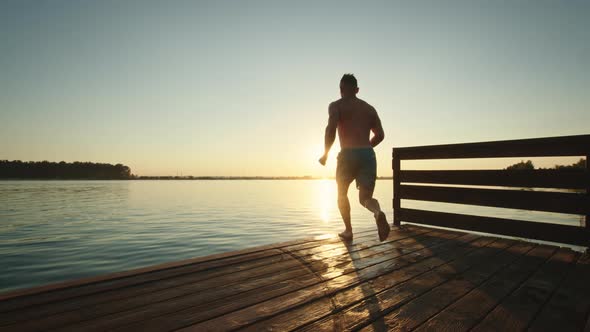 A Young Man is Running Down the Pier and Jumping Into the Lake in the Style of a Bomb alt
