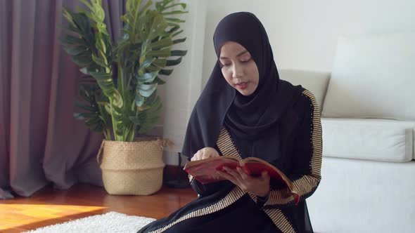 Young Muslim female wearing Islamic clothes reading the Quran alt