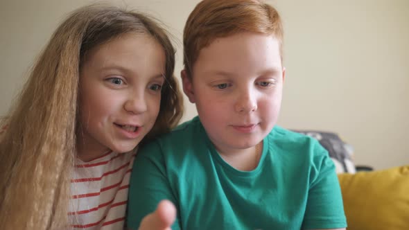 Joyful Small Boy and Girl Watch a Funny Video on Smartphone Sitting on the Sofa at Room alt