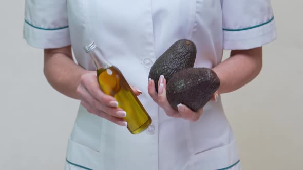 Nutritionist Doctor Holding Organic Avocado Fruit and Bottle of Oil alt