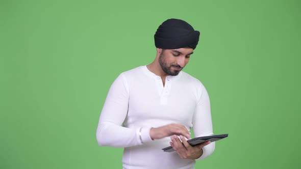 Young Happy Bearded Indian Man Using Digital Tablet and Getting Good News