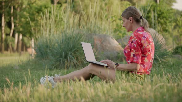 A Middleaged Woman Works Using Her Laptop in a Public Park alt