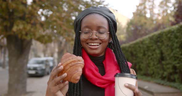 Young Black Girl with a Croissant in Her Hands in the Middle of the Street alt