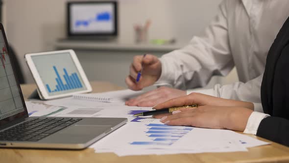 Man and Woman Viewing Papers with Charts and Graphs Using Laptop Tablet alt