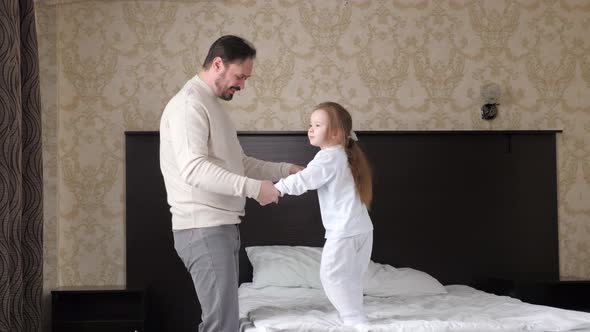 Happy Family Child Daughter and Dad Holding Hands Jumping on Bed alt