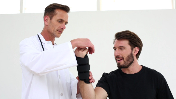 Doctor Checking On Injured Patient In Wrist Brace alt