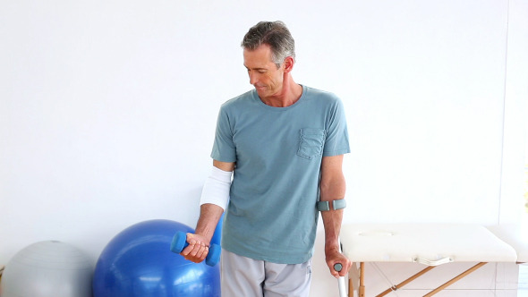 Injured Patient On Crutches Lifting Dumbbell