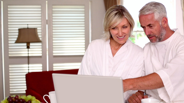 Happy Couple Using Laptop Together In Bathrobes